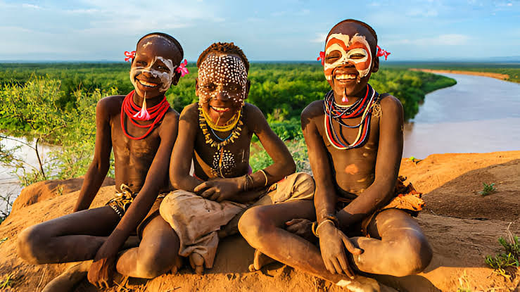Children smiling near a riverside landscape in southern Ethiopia